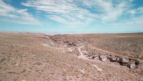 Drone-Volando-Sobre-El-Desierto-Chileno-Con-Una-Carretera-Remota-Con-Camiones-En-El-Fondo