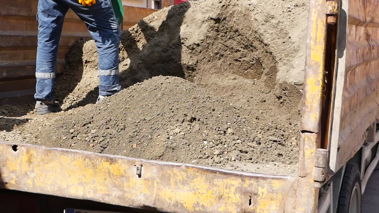un trabajador de la construcción excava grava en la cama de un camión
