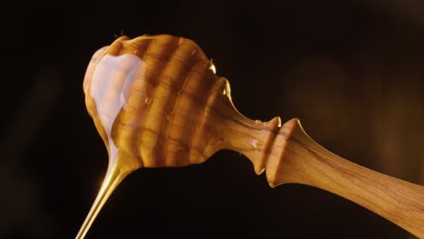 static shot of a spinning honey spoon on which honey is flowing against black background