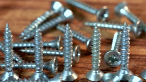 the bunch of steel screws on wooden table. screw production, heap of metal details, close up shot