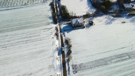 Aerial-view-of-a-van-driving-on-a-narrow-path-passing-by-a-farm-on-a-beautiful-winter-day,-Dalmatia,-Croatia