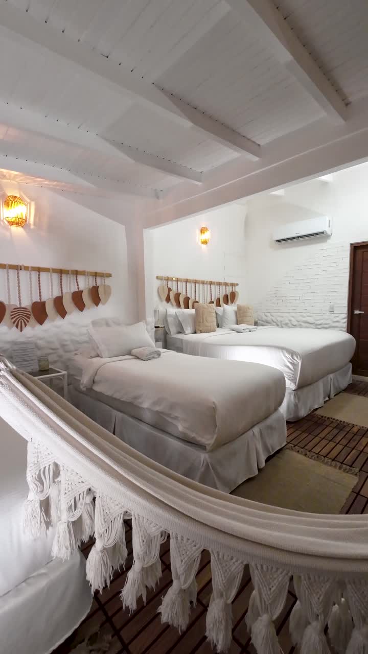 Tropical bedroom with three neat white beds, wooden floor, white and brown decor, and a hanging hammock in bright natural light.
