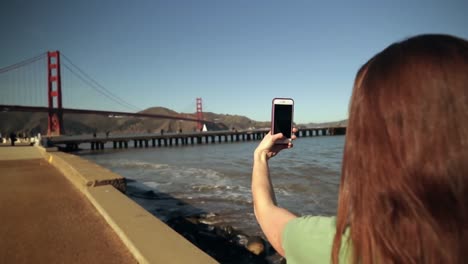 mujer tomando una foto del puente golden gate con un teléfono inteligente