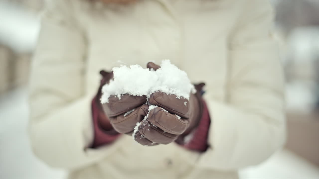 Bright snowflakes cover the ground while hands gather fresh snow to create a snowball. The cold winter day is peaceful, showcasing the beauty of a snowy season