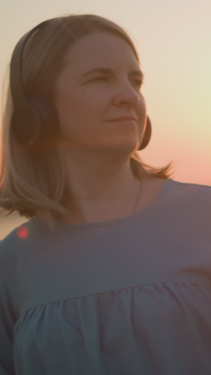 una mujer con auriculares sonríe satisfecha mientras mueve suavemente su cuerpo como si estuviera bailando. se baña en la cálida luz dorada del sol poniente, creando una atmósfera pacífica y alegre
