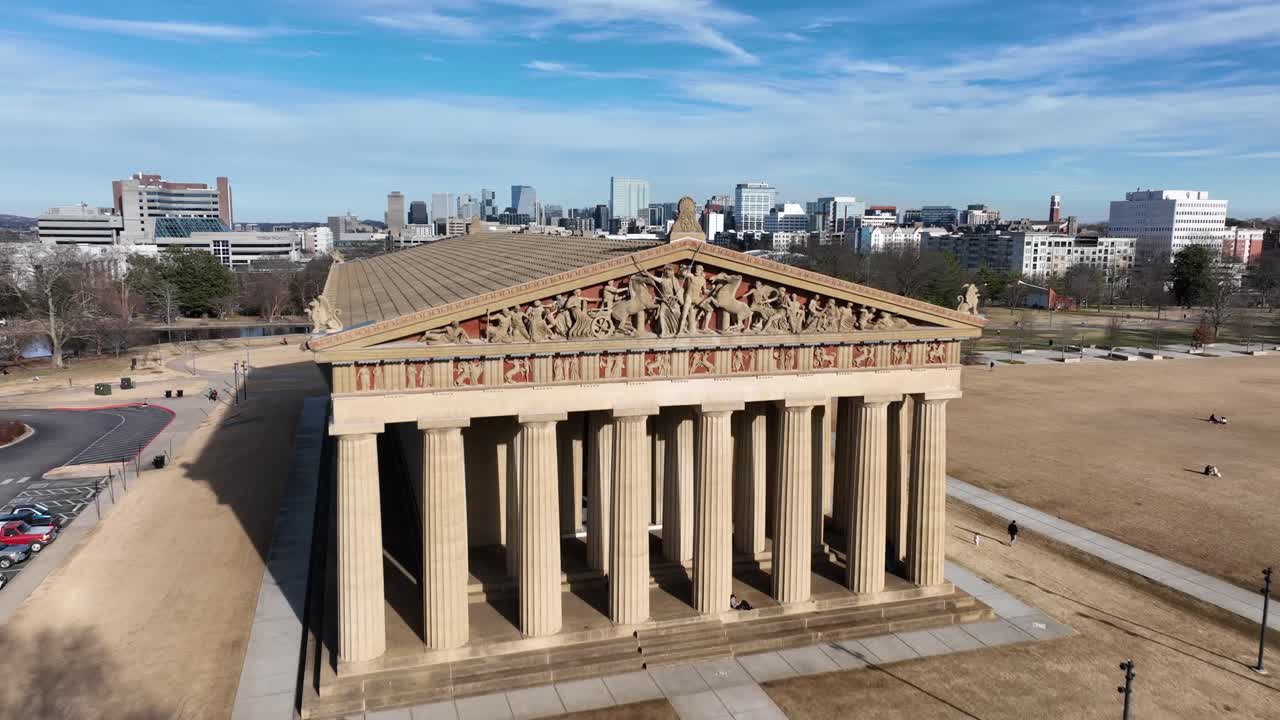 Stigande flygbild över Nashville Parthenon vintertid, med stadens silhuett i bakgrunden under klarblå himmel vid Centennial Park, Tennessee. Tennisbanor och en lugn damm i parken. Solig dag.