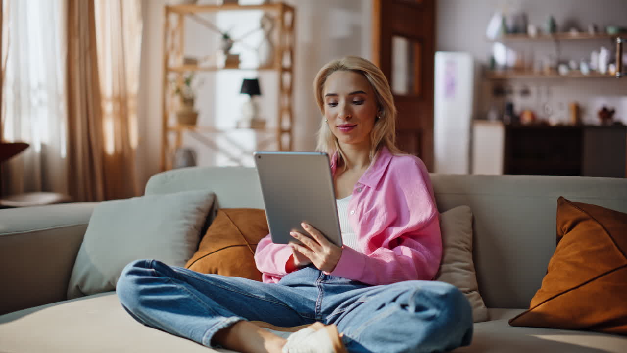 Blonde woman surfing tablet internet sitting at home couch. Lady browsing pad