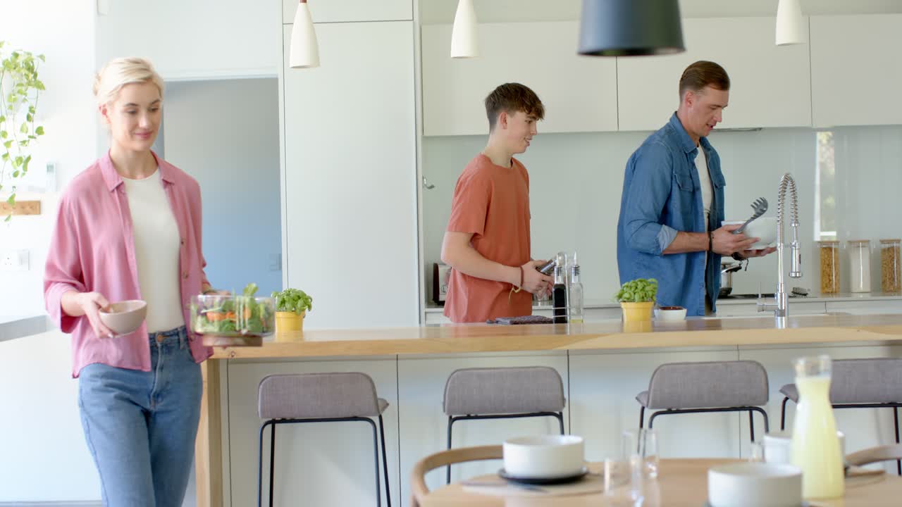 Vanhemmat ja teini-ikäinen poika valmistavat ateriaa keittiössä naisen astuessa sisään lasinen salaattikulho mukanaan.