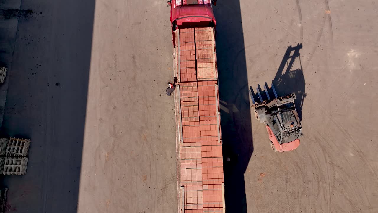 Overhead shot of piles of red bricks on construction site being loaded on lorries