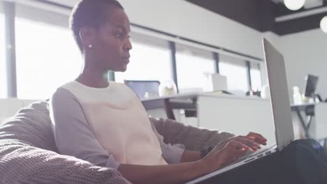 african american businesswoman sitting in armchair and using laptop