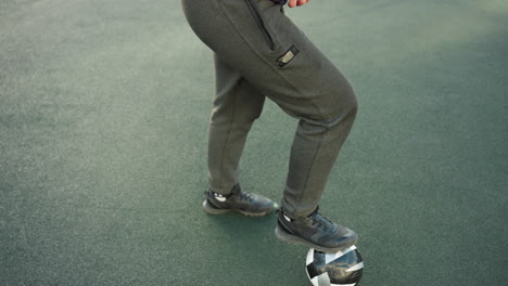 close-up of an athlete's legs wearing sporty sneakers with one foot resting on a soccer ball, showcasing a moment of readiness and control on a green sports field under natural lighting