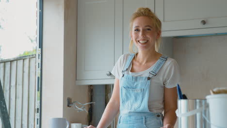 portrait of smiling woman wearing dungarees renovating kitchen at home