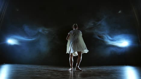 elegant ballerina jumping and dancing in barefoot and white loose oversize dress in studio. with smoke.