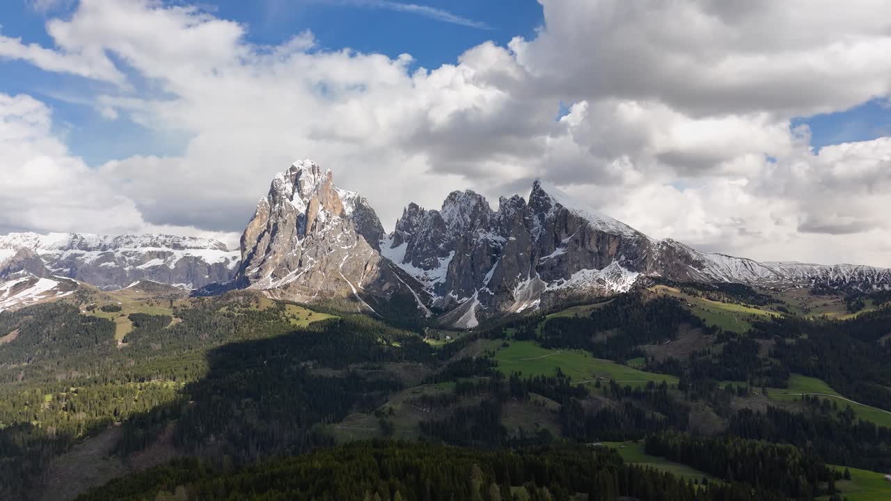 Aerial view of Seiser Alm with snow-capped Sassolungo mountains, lush meadows, and scattered forests in the rugged alpine terrain of the Dolomites