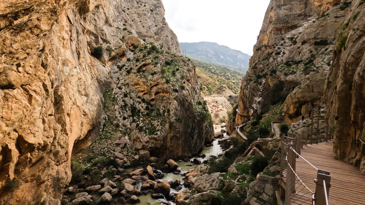 toma 4k de turistas caminando por un sendero de madera entre acantilados con río de montaña debajo en el caminito del rey en gorge chorro, provincia de málaga, españa