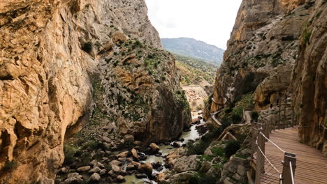 4k-Shot-of-tourists-walking-on-a-wooden-trail-between-cliffs-with-mountain-river-under-at-El-Caminito-del-Rey-in-Gorge-Chorro,-Malaga-province,-Spain