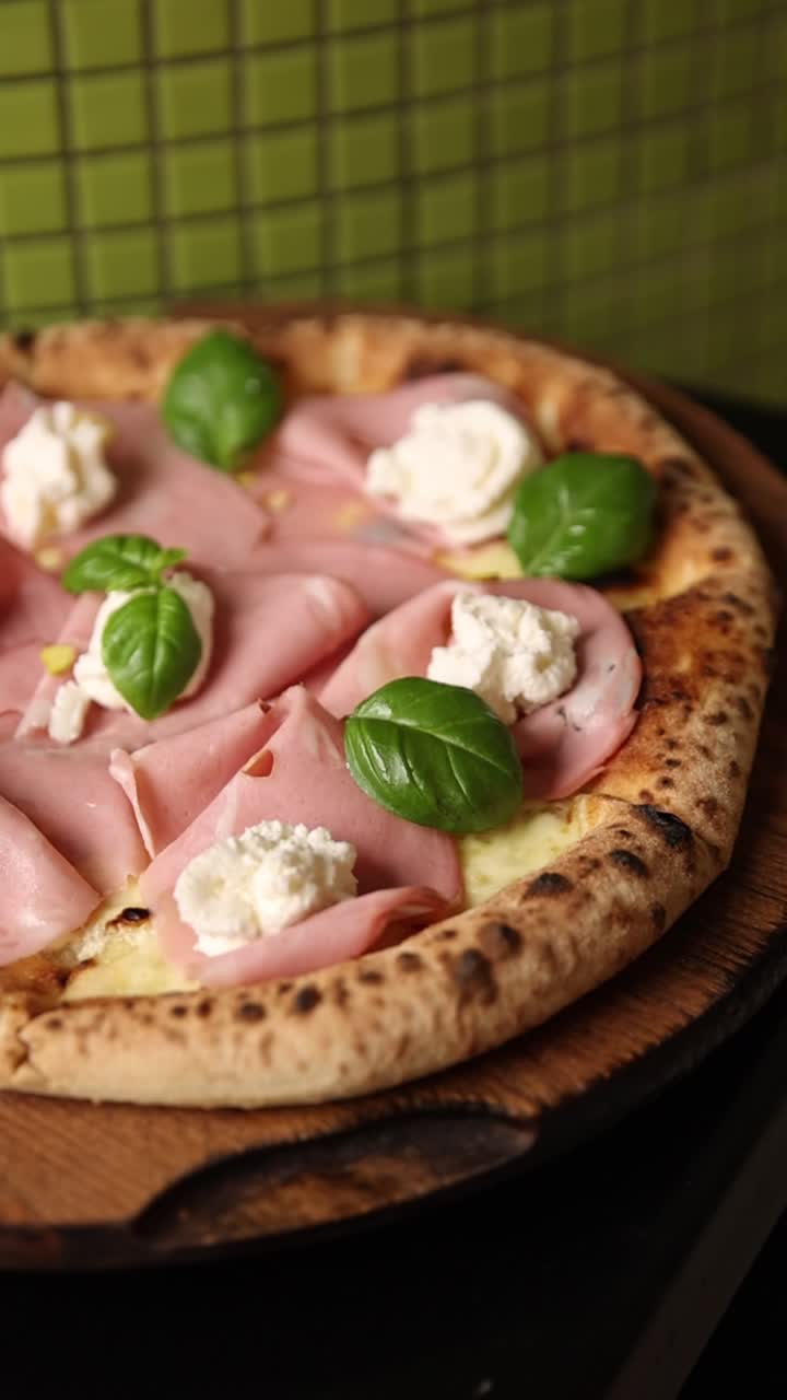 Pizza gourmet con mortadella e ricotta guarnita a mano con basilico fresco