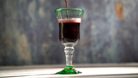 seamless, looping clip of red wine pouring into a rustic glass with blue background