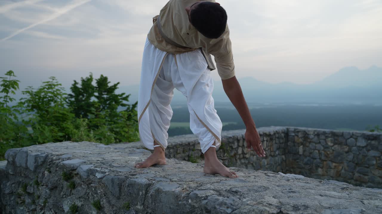 hombre que se levanta de la postura de hatha yoga en la cima de la colina con ruinas del castillo al amanecer