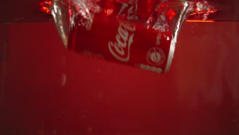Coca Cola can falls into water in a small aquarium in slow motion with a red background for use in advertisements