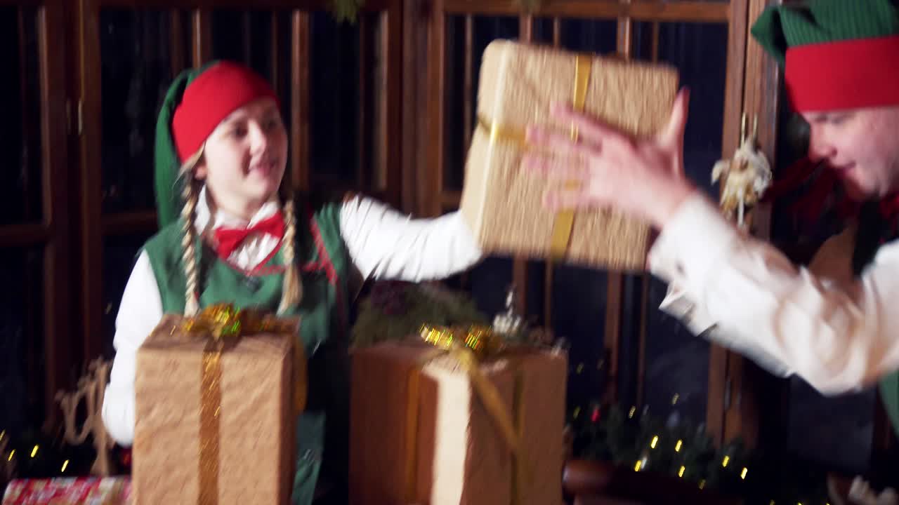 Excited elves and presents for Christmas. Funny female and male elves putting gift boxes on the table. Christmas decorated room background