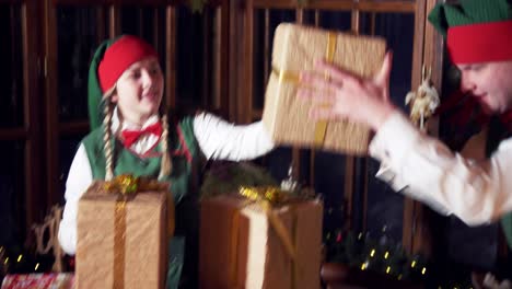 excited elves and presents for christmas. funny female and male elves putting gift boxes on the table. christmas decorated room background