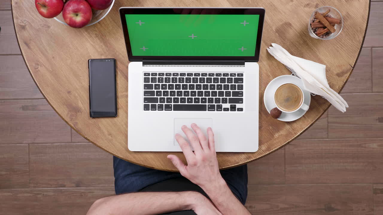 Laptop with green screen on a table with coffee and apples