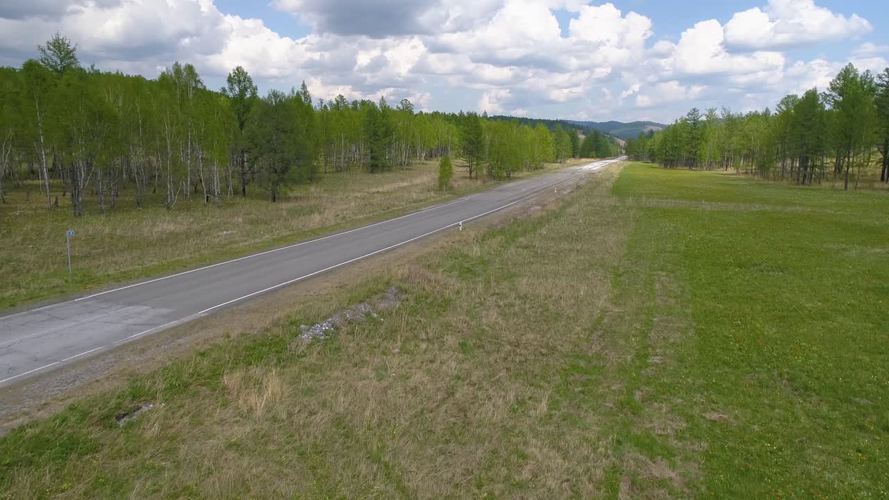 un camión blanco conduciendo en una carretera de campo vacía con campos verdes y bosques a cada lado.