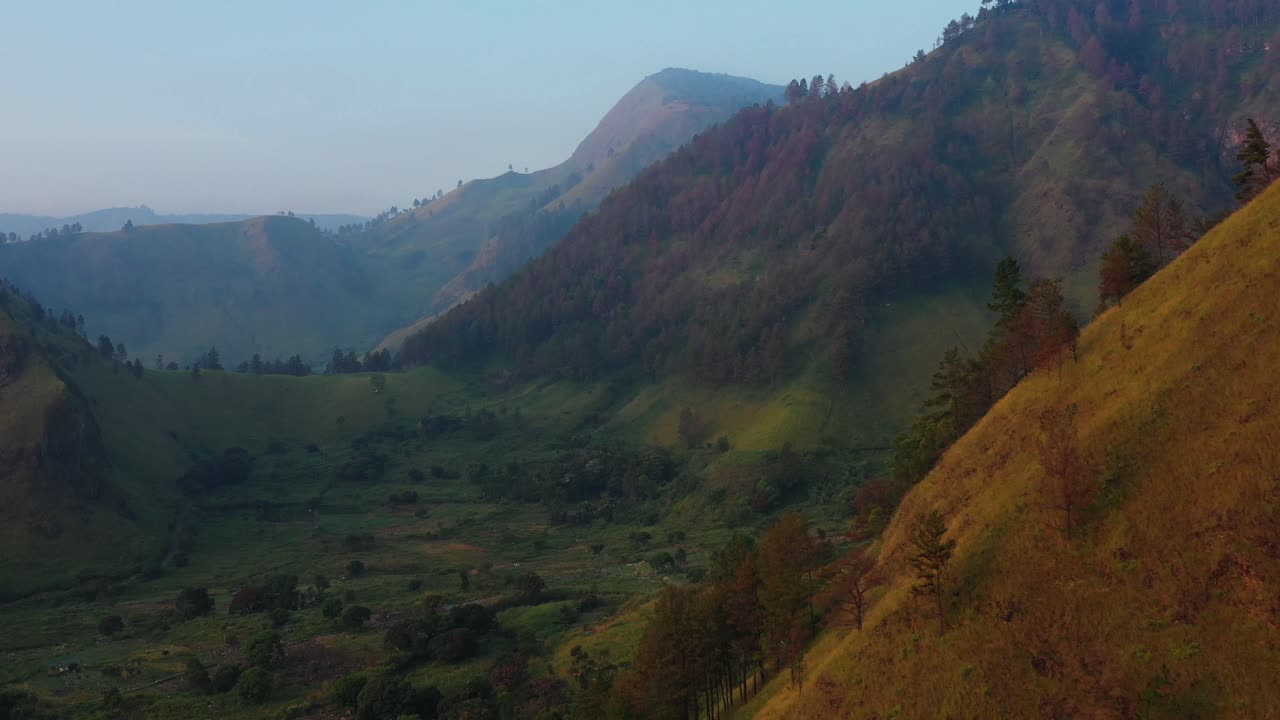 Rekaman drone udara yang bergerak menjauh, memperlihatkan tebing dan lembah yang rimbun saat senja di Kabupaten Karo, Sumatera Utara, Indonesia.