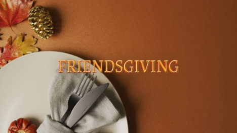 animation of friendsgiving text over cutlery and autumn leaves over brown background