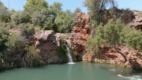 Man-swan-dives-into-water-towards-scenic-waterfall-in-algarve-portugal,-drone