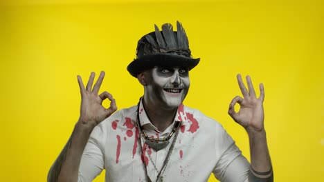 hombre siniestro con horrible esqueleto de halloween caras de maquillaje, mirando a la cámara, mostrando el signo ok
