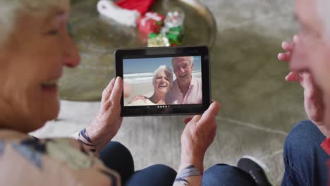 pareja caucásica mayor usando una tableta para una videollamada de navidad con una pareja feliz en la pantalla