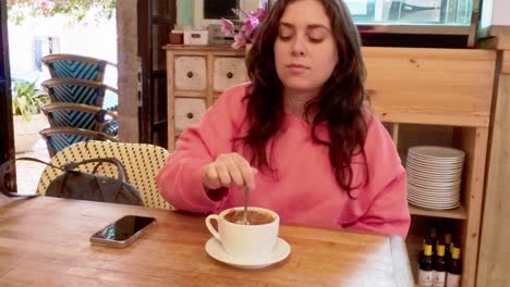 a woman is sitting at a table with a cup of coffee and a cell phone