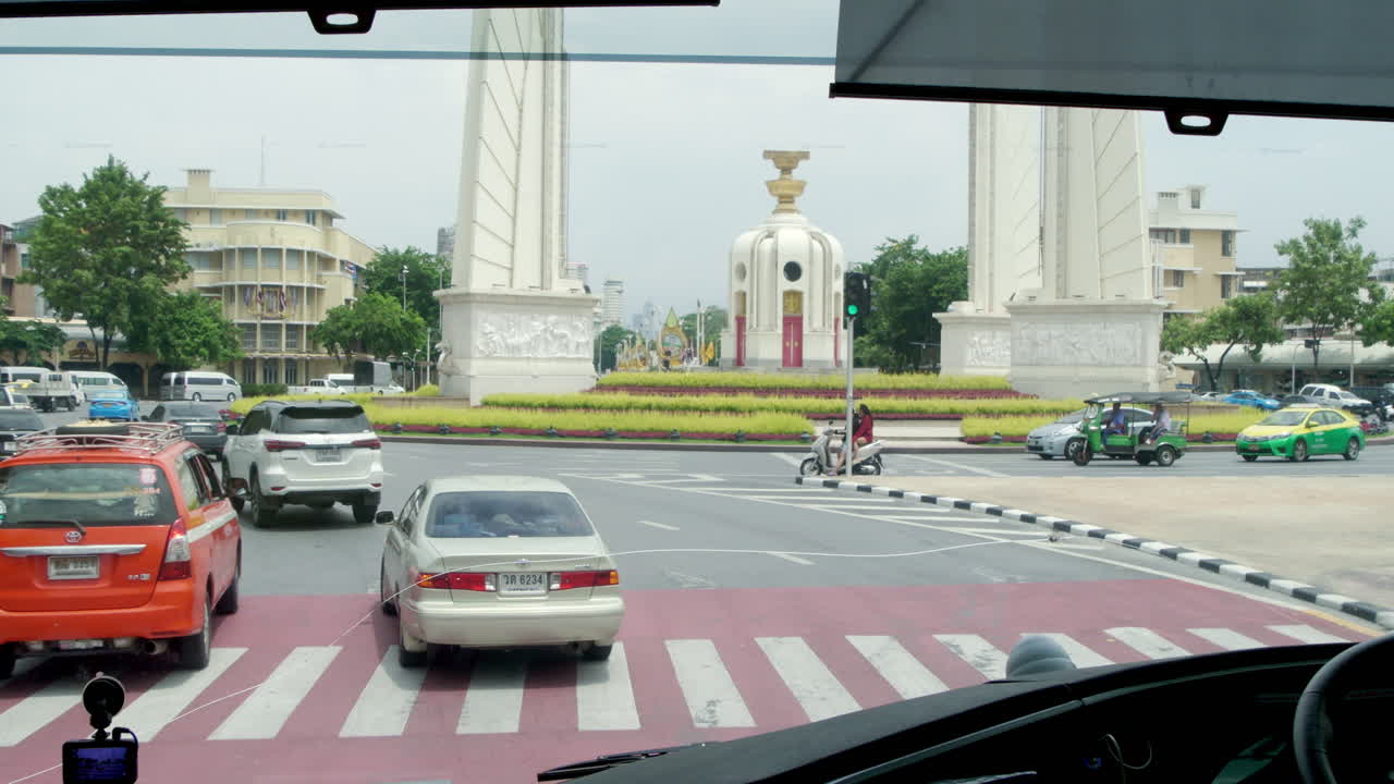 Tourist bus passing the Democracy Monument in Bangkok amidst heavy traffic. Experience the vibrant energy of the city as locals commute and travelers explore iconic landmarks.