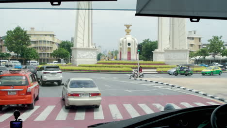 tourist bus passing the democracy monument in bangkok amidst heavy traffic. experience the vibrant energy of the city as locals commute and travelers explore iconic landmarks.