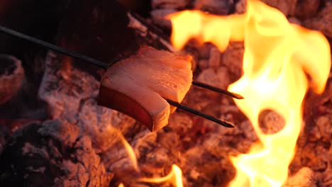 Liquid-fat-dripping-on-campfire-from-a-bacon-on-a-fork-skewer-at-a-barbecue---180-fps-slow-motion