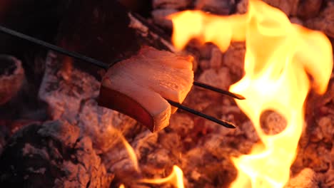 liquid fat dripping on campfire from a bacon on a fork skewer at a barbecue - 180 fps slow motion