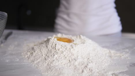 close up view of female hands breaking the egg into flour on the kitchen table. slow motion shot