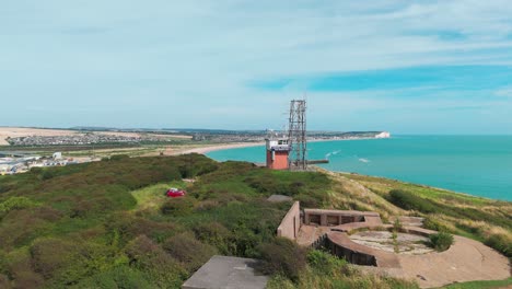 a grassy coastal hill with a small structure overlooking the sea on a bright day, aerial view