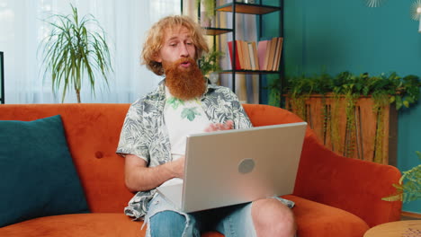 hombre sentado en el sofá de casa, mirando a la cámara, haciendo una llamada de videoconferencia con amigos o familiares