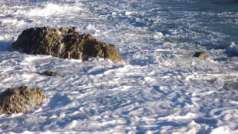 las olas del mar salpicando furiosamente en el acantilado sumergido en la playa, espumando y repitiendo la energía de la naturaleza