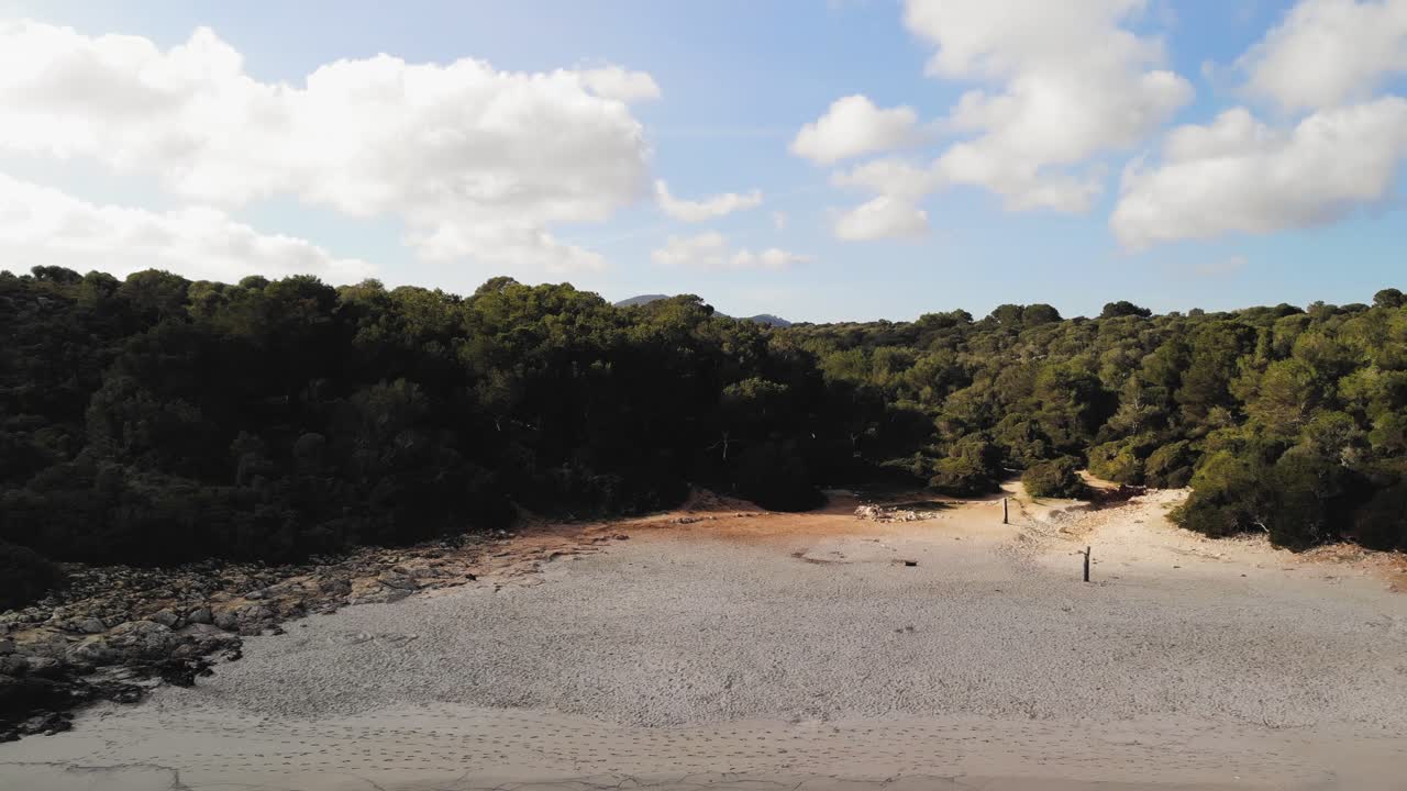 aerial drone shot of the mountain landscape of Majorca, panning down to focus on a small hidden beach nestled in the trees on the coast of the Mediterranean