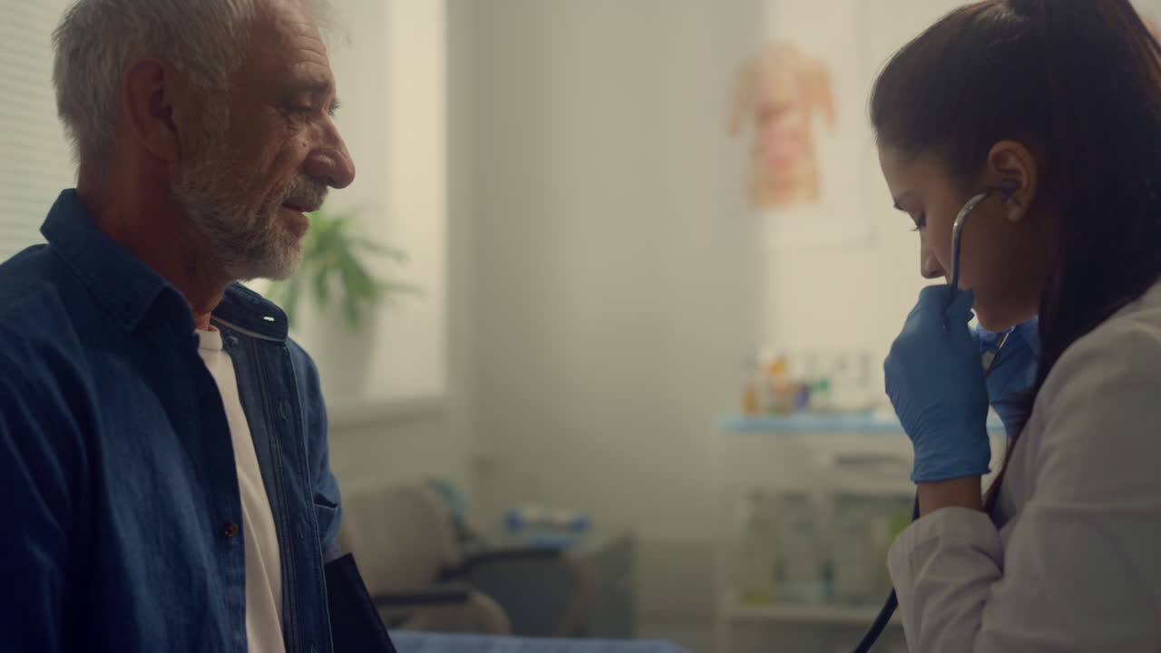 Kvinnelig terapeut sjekker pulsen til en eldre pasient på klinikken med stetoskop