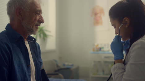 woman therapist checking pulse elderly patient in clinic using stethoscope.