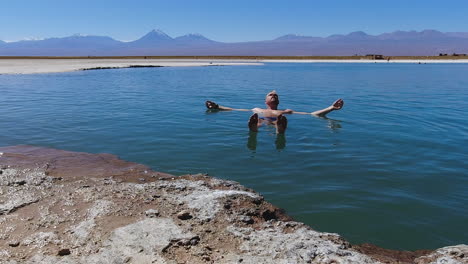 man enjoys sunny swim in extra buoyant saline laguna piedra in chile