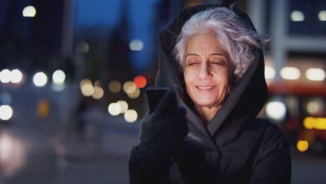 Mature-Woman-On-City-Street-At-Night-Ordering-Taxi-Using-Mobile-Phone-App