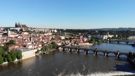 Aerial-flyover-over-Vltava-river-in-Praha,-Czech-Republic-with-a-view-of-the-Charles-Bridge-and-the-Prague-Castle-on-a-sunny-morning