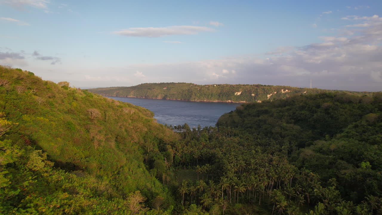 avión volando cerca de los árboles de la selva tropical en un valle al amanecer con una vista de la playa de la bahía de gamat en nusa penida, bali, indonesia