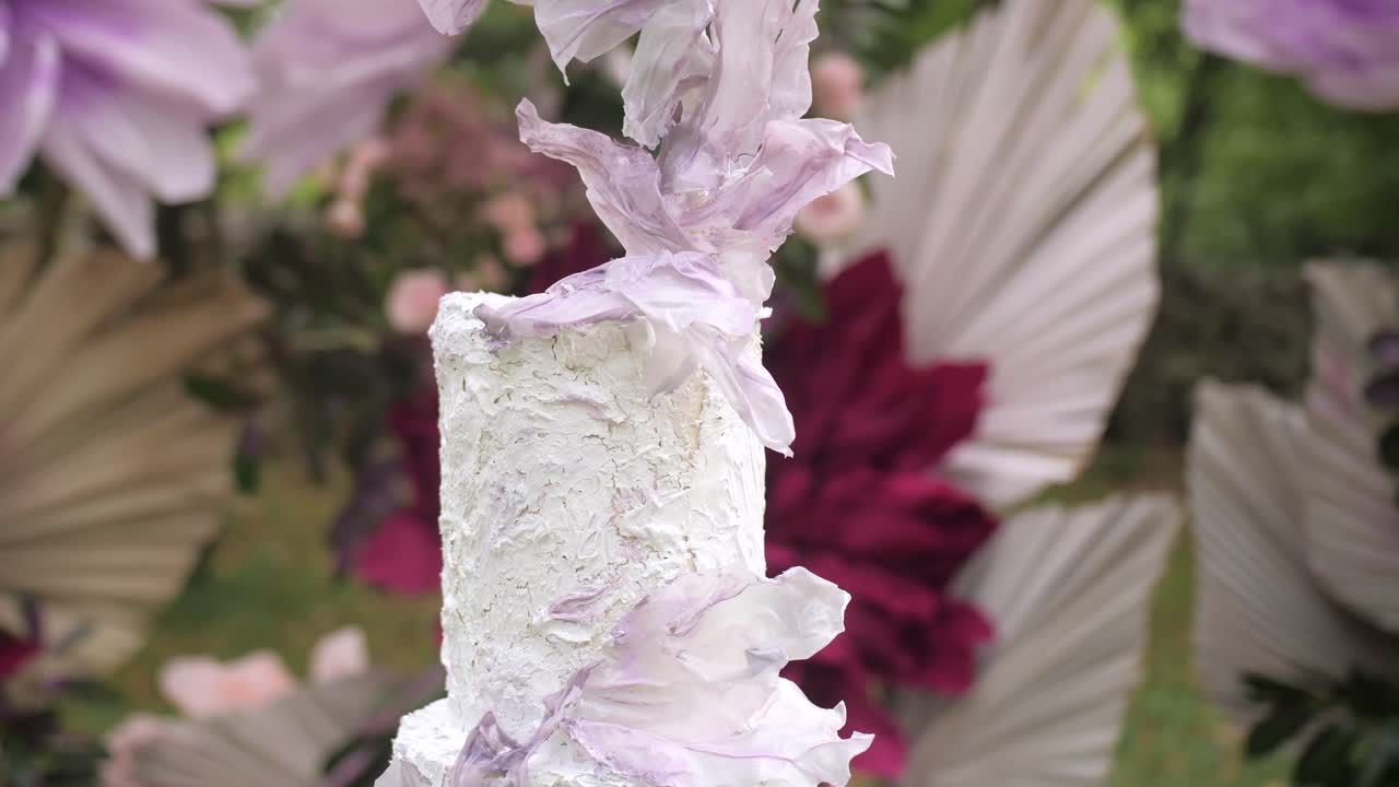artistic wedding cake closeup tilt, arch of lilac crepe flowers and roses in the background.